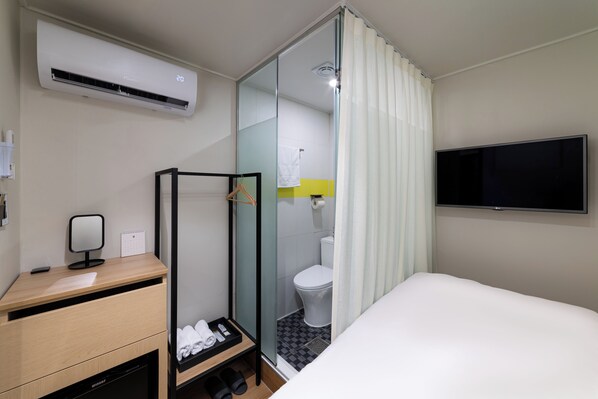 A hotel room with a bed, a desk with a calendar, a TV, a shower area, and a toilet.