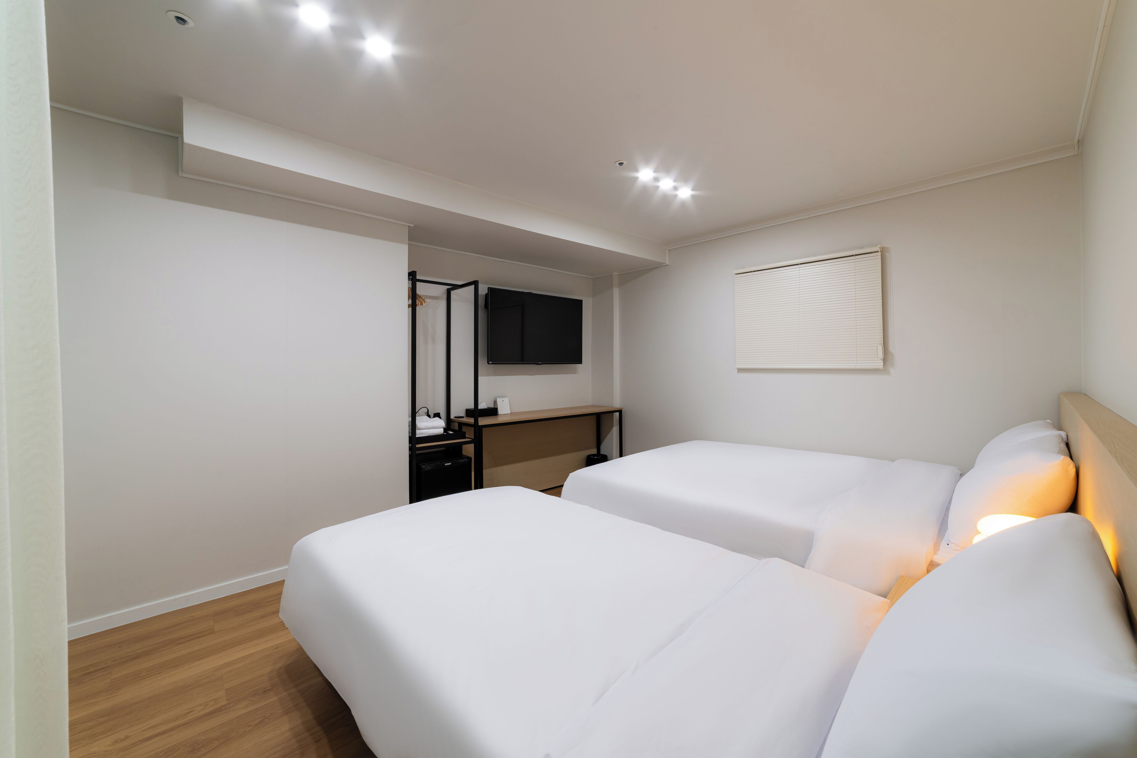 A hotel room with two beds, a desk, a TV, and a window with blinds.