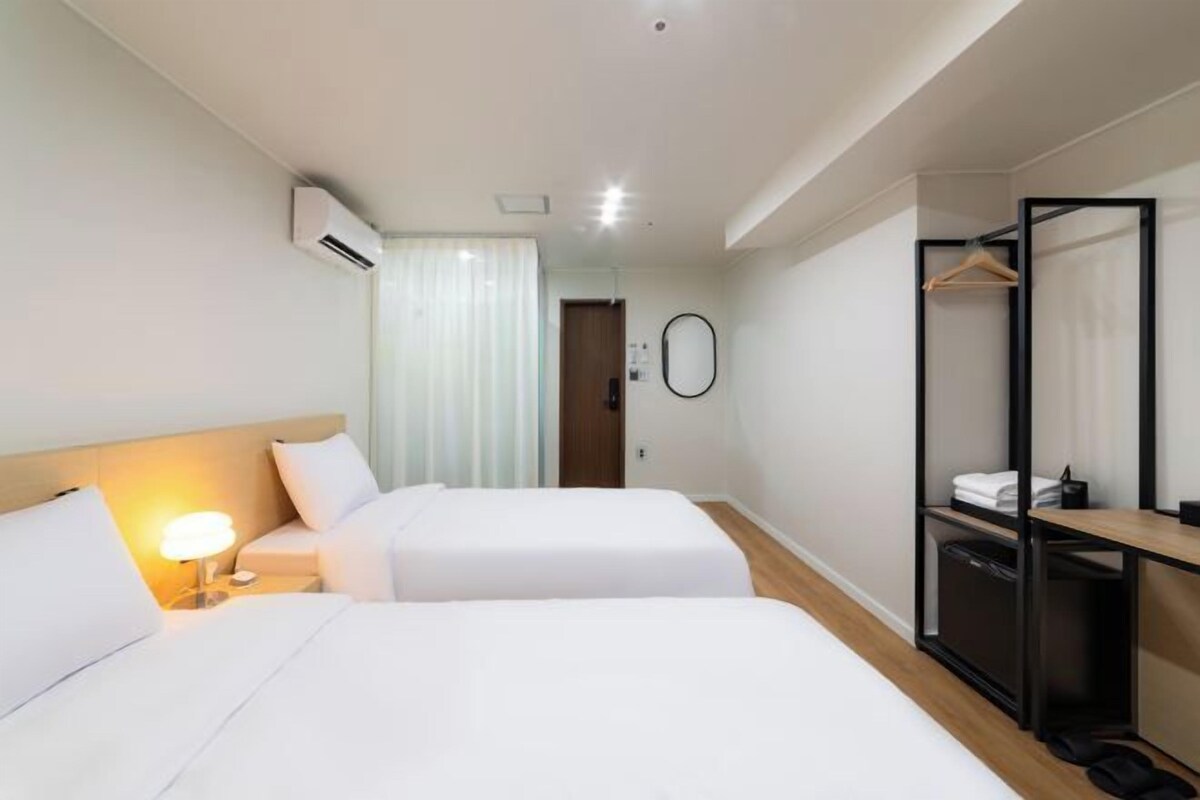 A hotel room with two beds, a desk, a wardrobe, and a mirror.