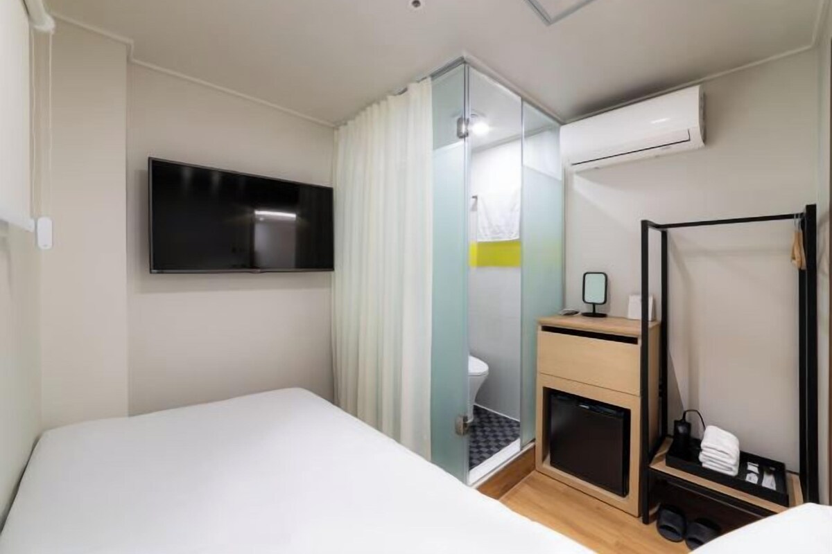 A hotel room with a bed, a television, a shower, and a small desk with a mirror.