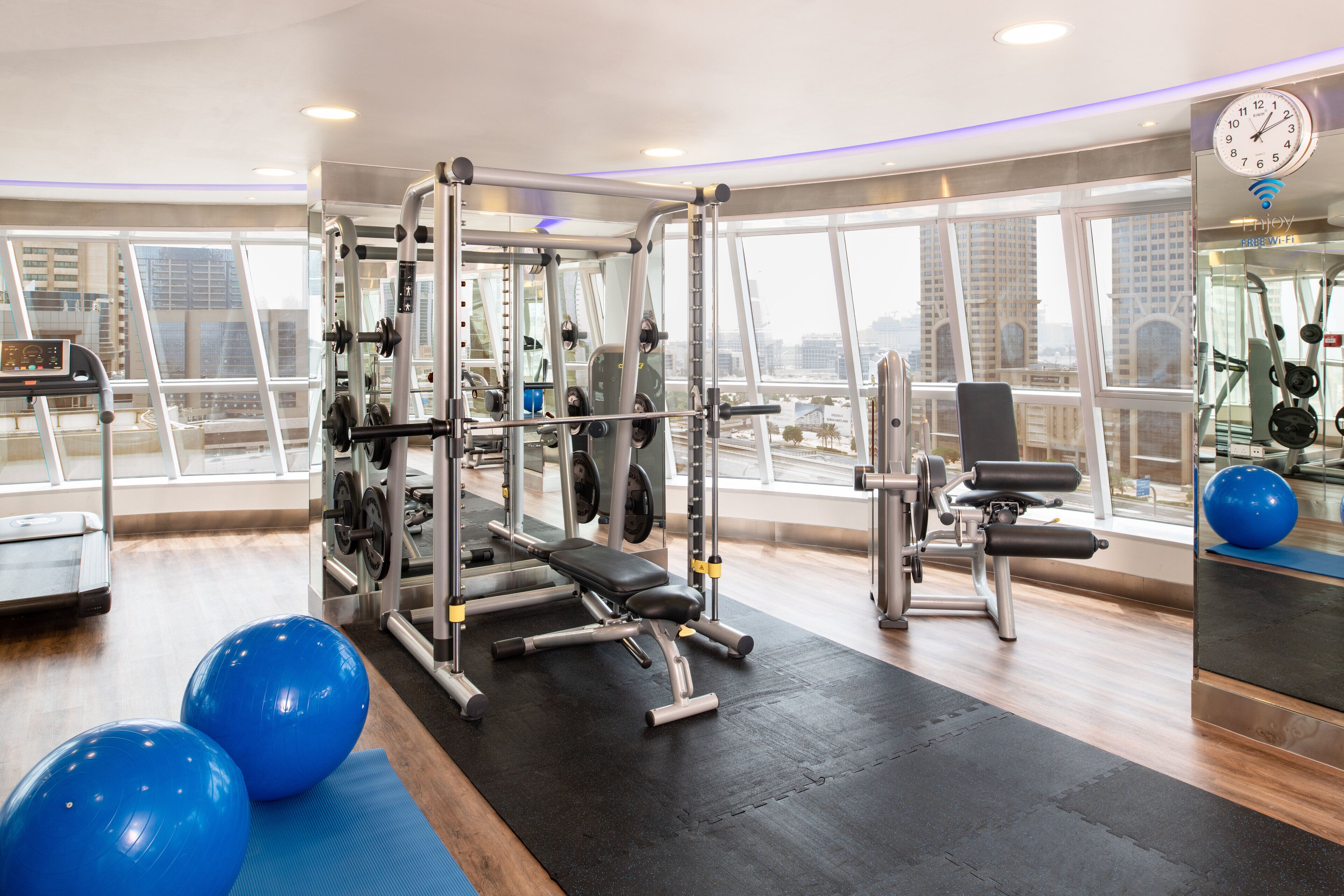 Une salle de sport équipée de matériel d’exercice, dotée de grandes fenêtres et offrant une vue sur les bâtiments.