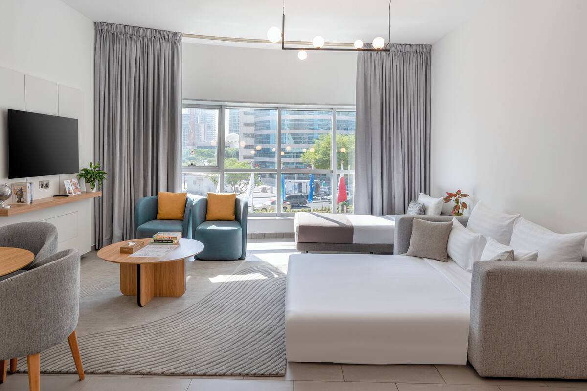 A modern hotel room with a large bed, a sofa, a coffee table, and a TV.