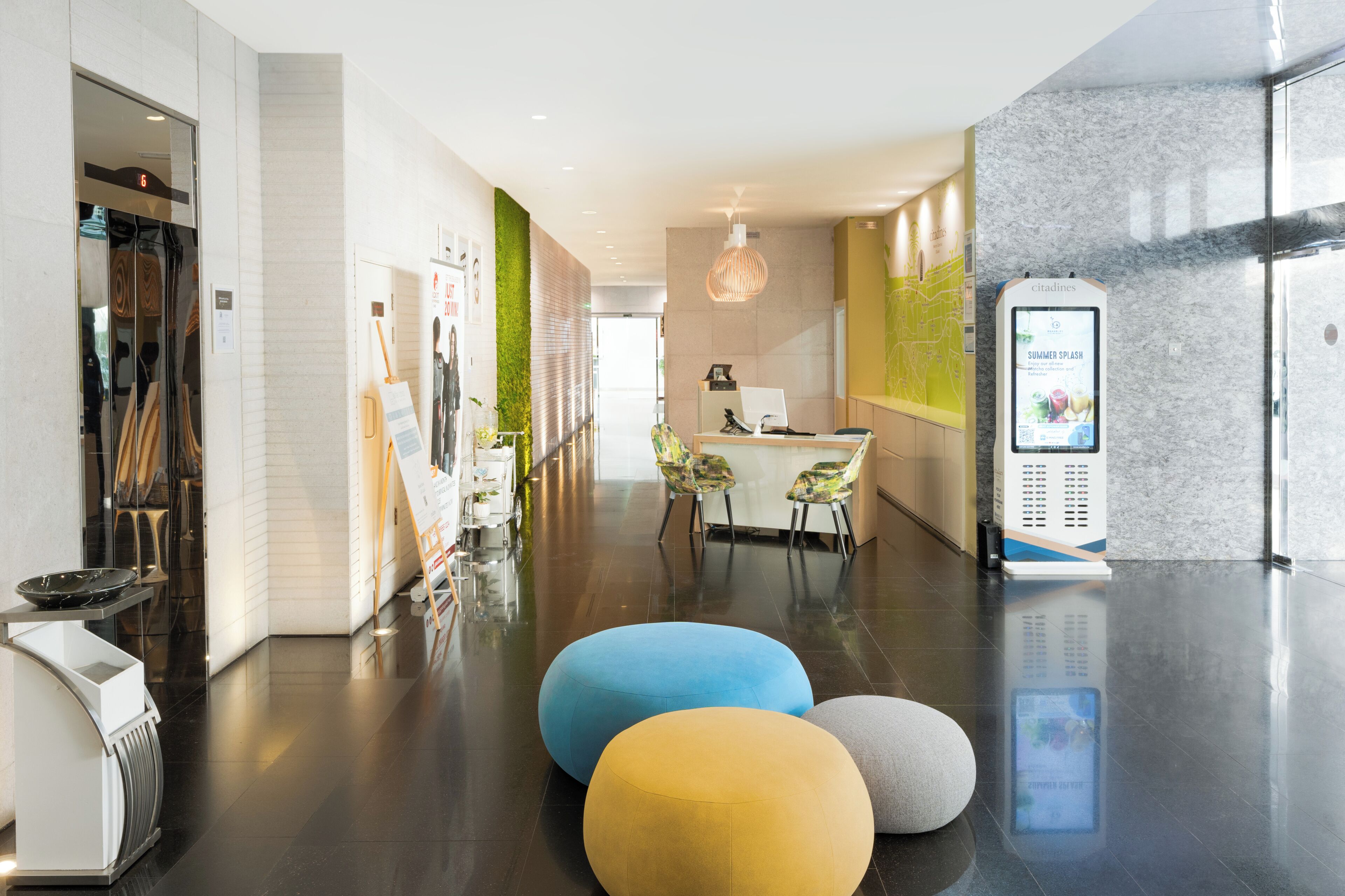 Recepció moderna d'hotel amb taulell d'informació, zona de seients i una quiosca d'informació digital.