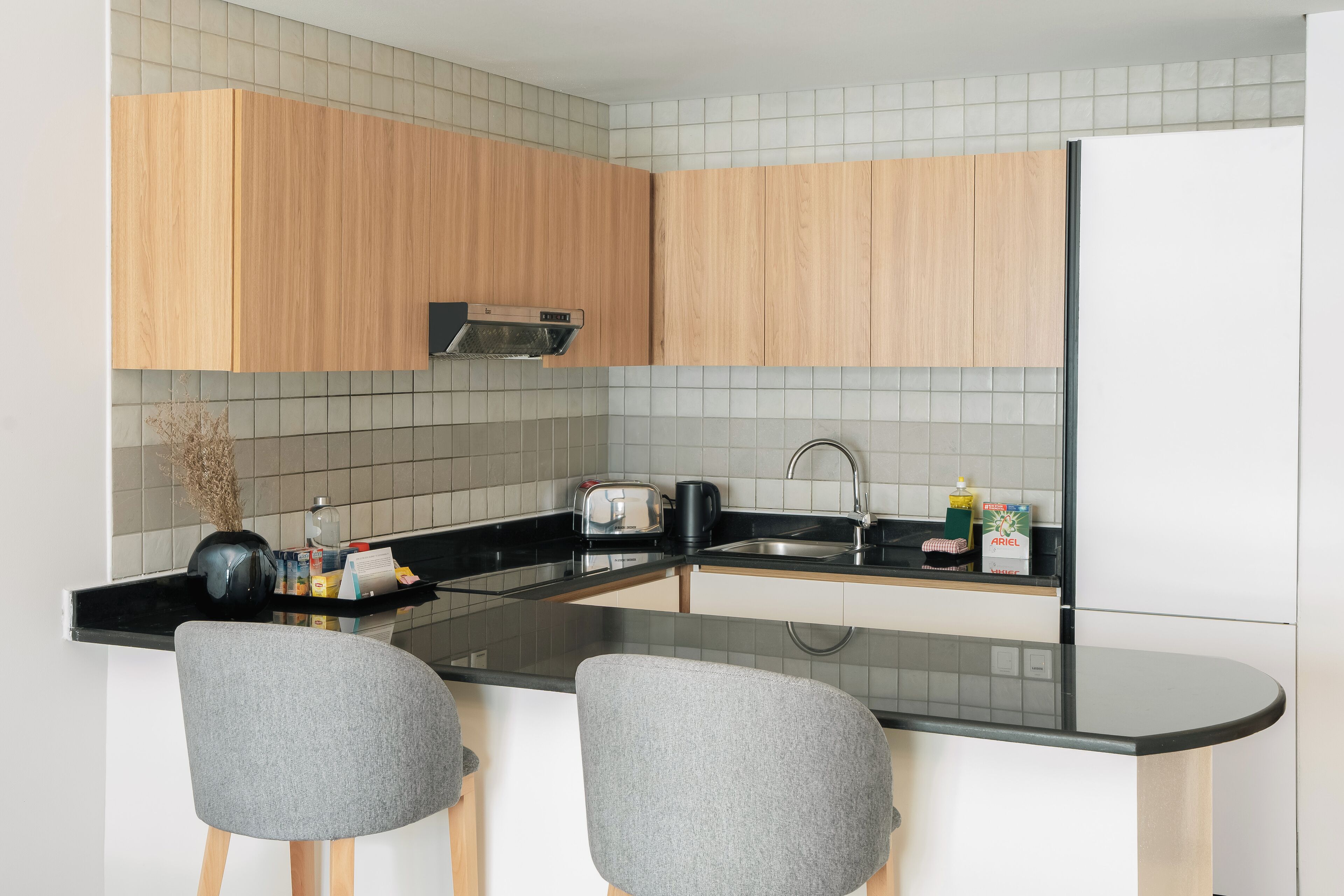 A modern kitchen with wooden cabinets, a black countertop, and two grey chairs.