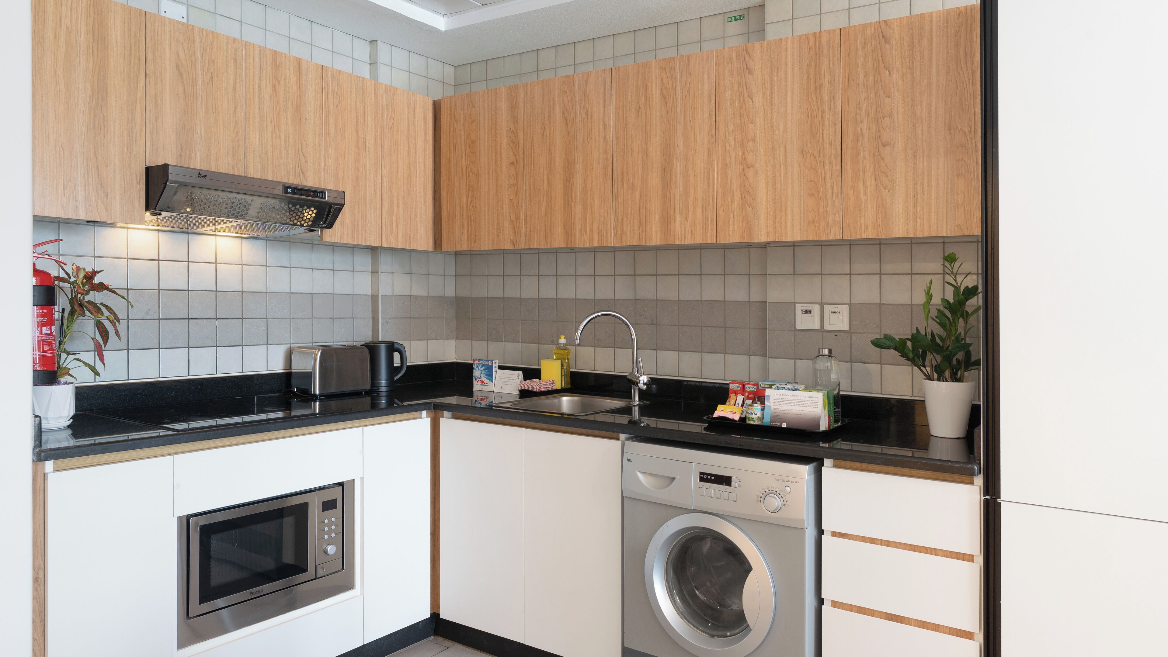A compact kitchen with a microwave, toaster, sink, and built-in washing machine.