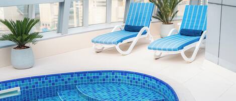 A modern indoor pool area with blue-tiled steps and lounge chairs.
