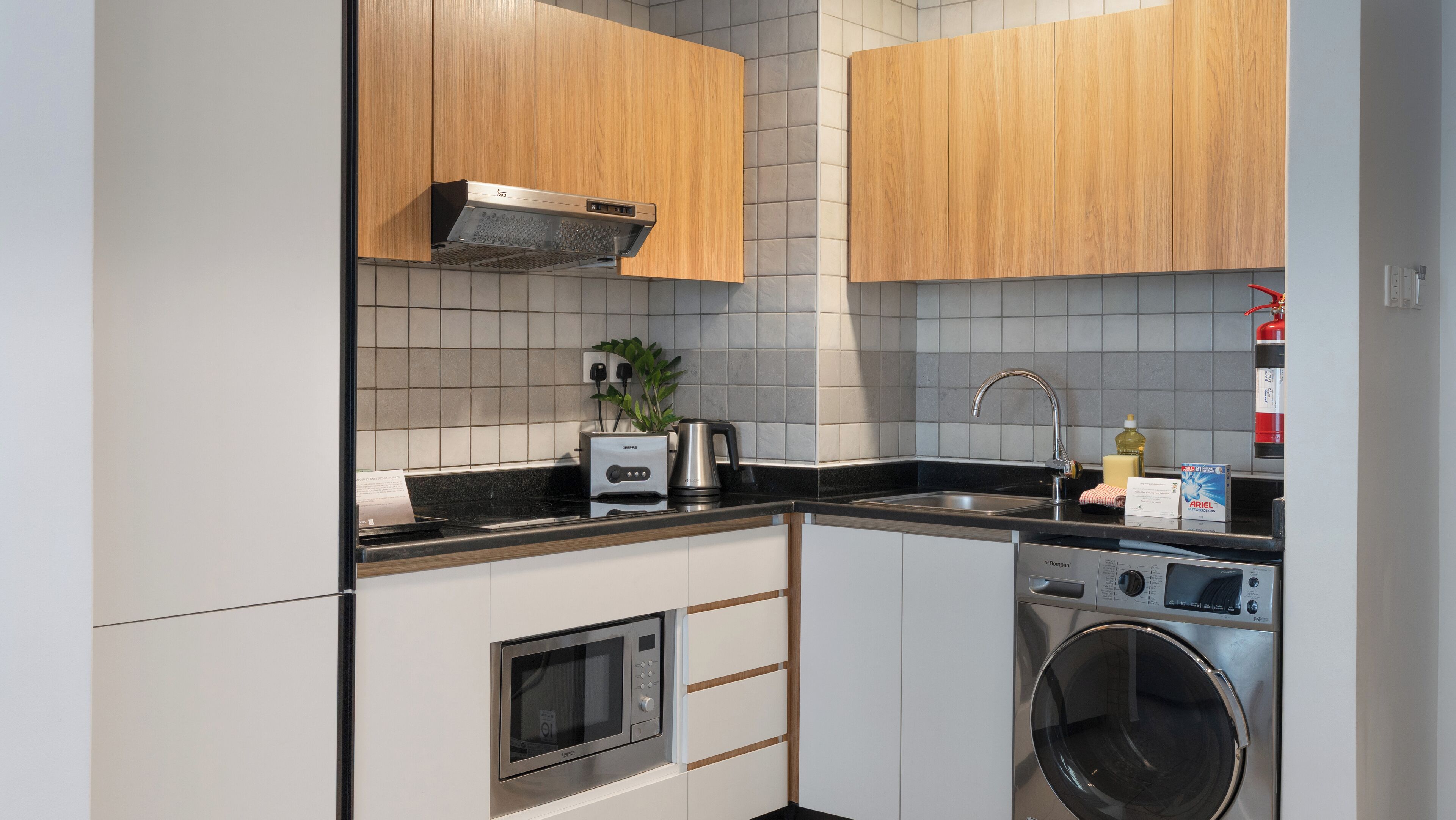 Een kleine keuken met een magnetron, broodrooster, spoelbak en een ingebouwde wasmachine.