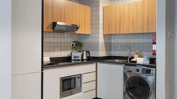 Een kleine keuken met een magnetron, broodrooster, spoelbak en een ingebouwde wasmachine.