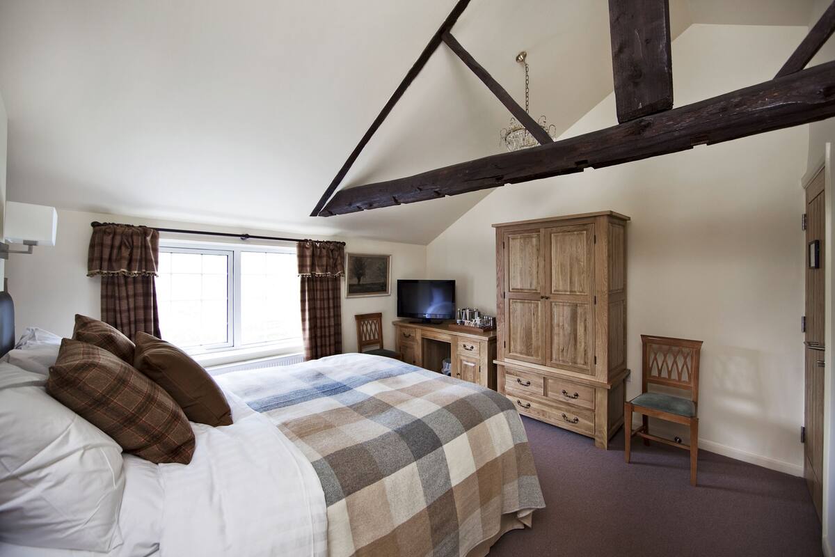 A bedroom with a large bed, a wooden wardrobe, a television, and a window with curtains.