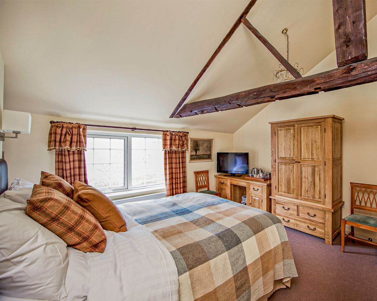 A bedroom with a bed, a wooden wardrobe, a television, and a desk.