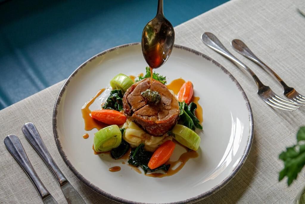 A plate of food with a spoonful of sauce being lifted, accompanied by vegetables and a piece of meat.
