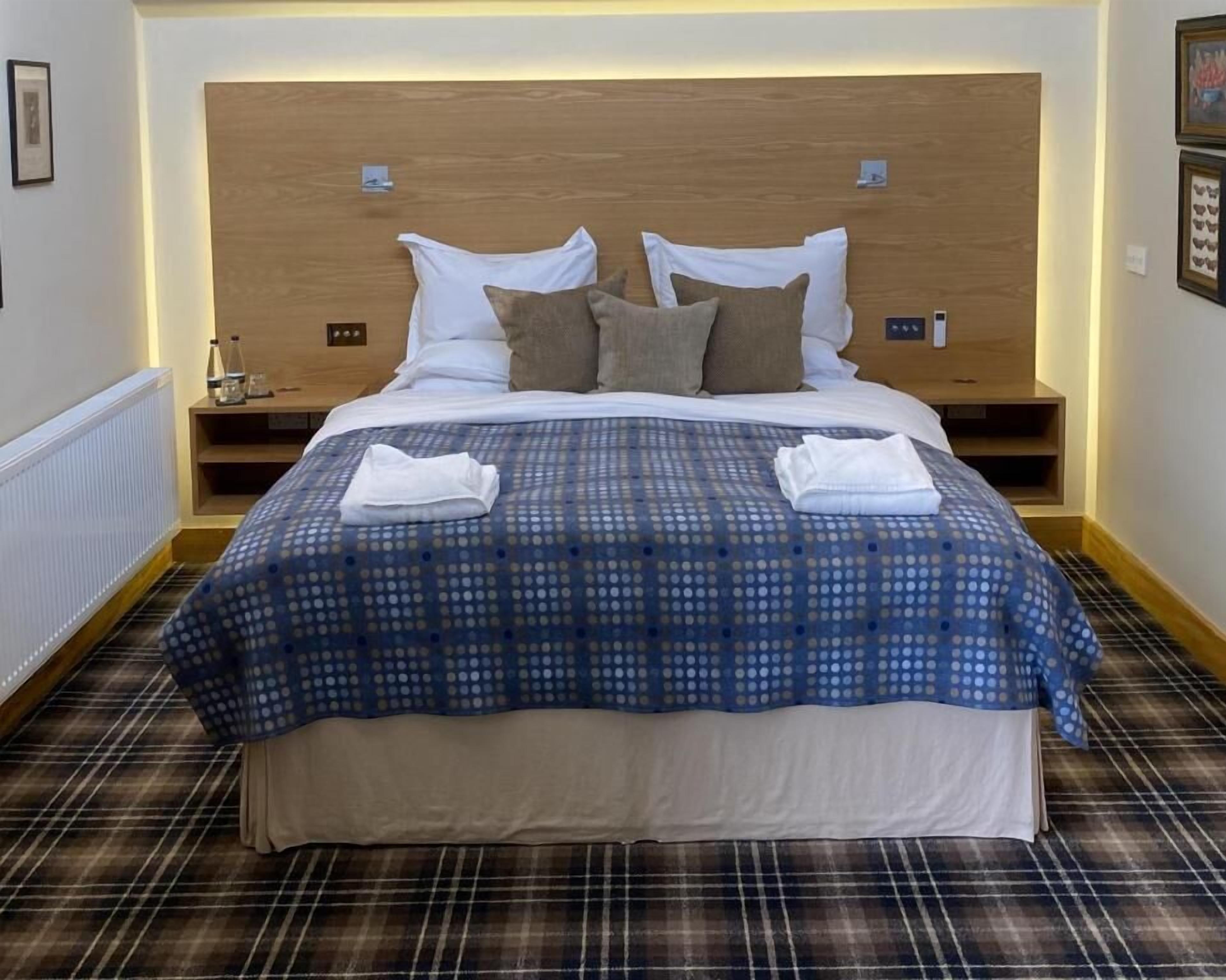 A neatly made bed with a blue and white polka dot bedspread, two pillows, and two folded towels.