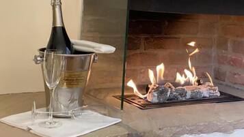 Eine Champagnerflasche in einem Eimer mit Gläsern auf einem Tisch neben einem Kamin mit brennenden Holzscheiten.