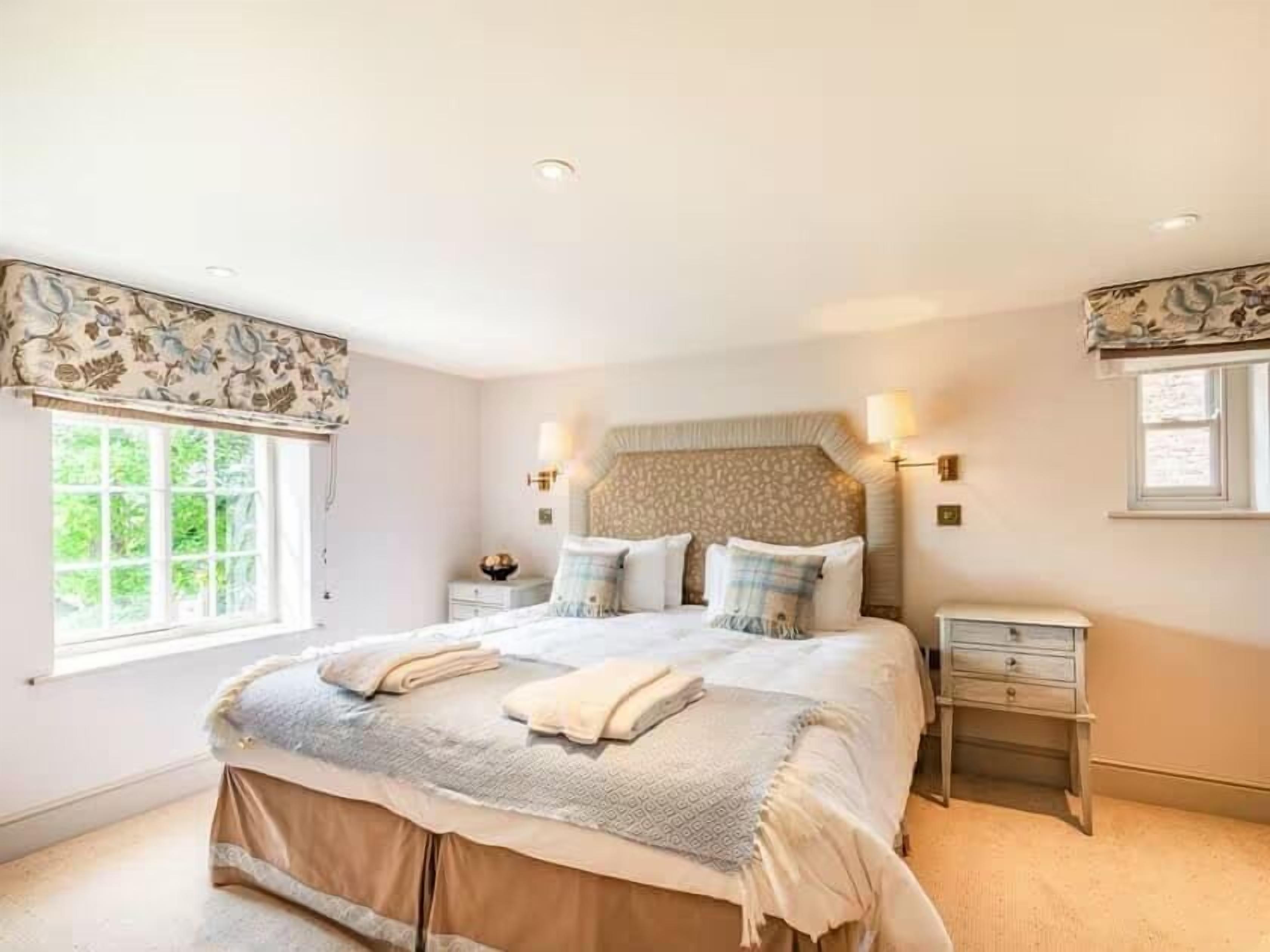 A bedroom with a large bed, bedside tables, a window with curtains, and a headboard with wall-mounted lights.