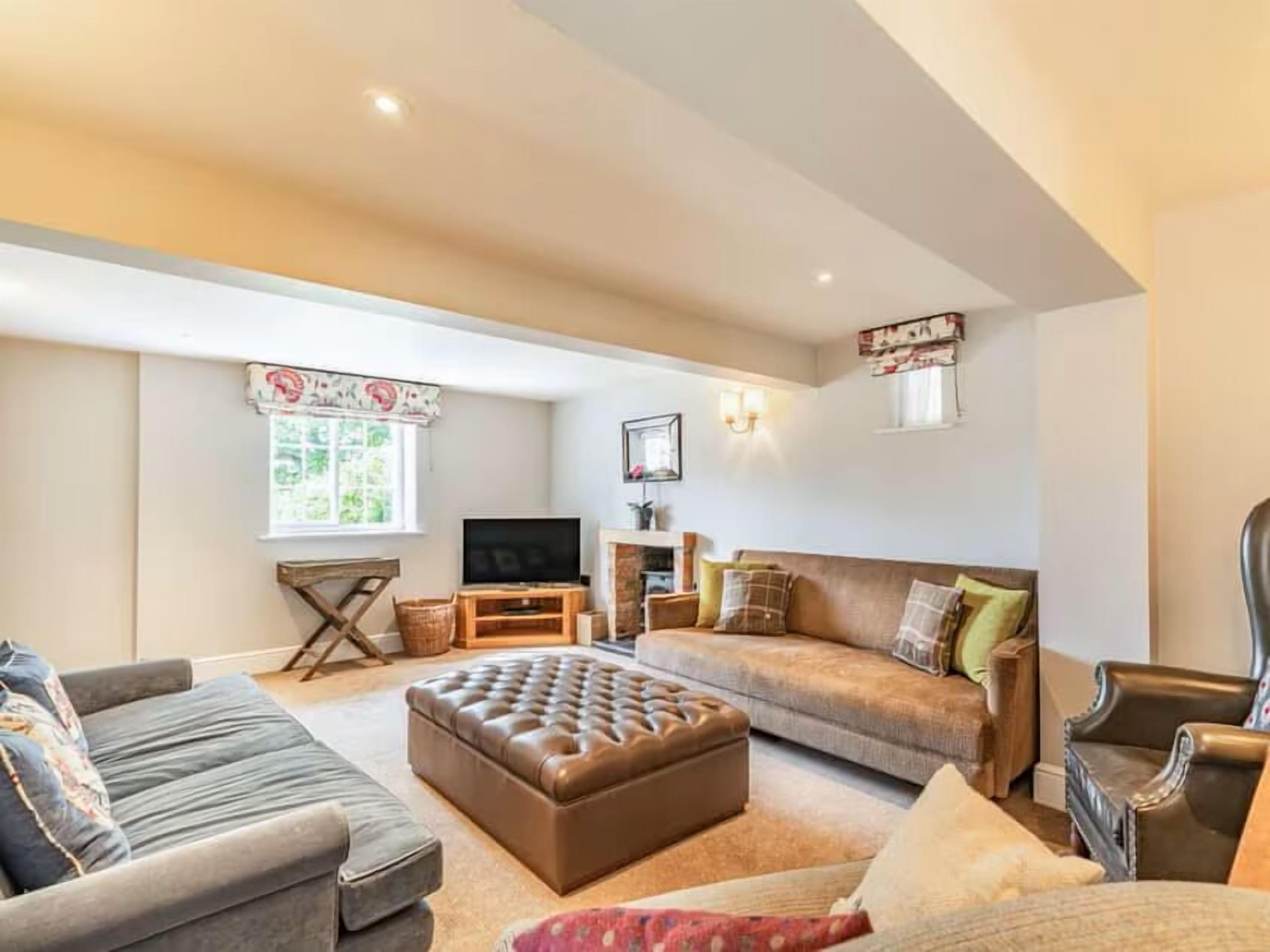 Una sala de estar con sofá, reposapiés, sillón y televisor.