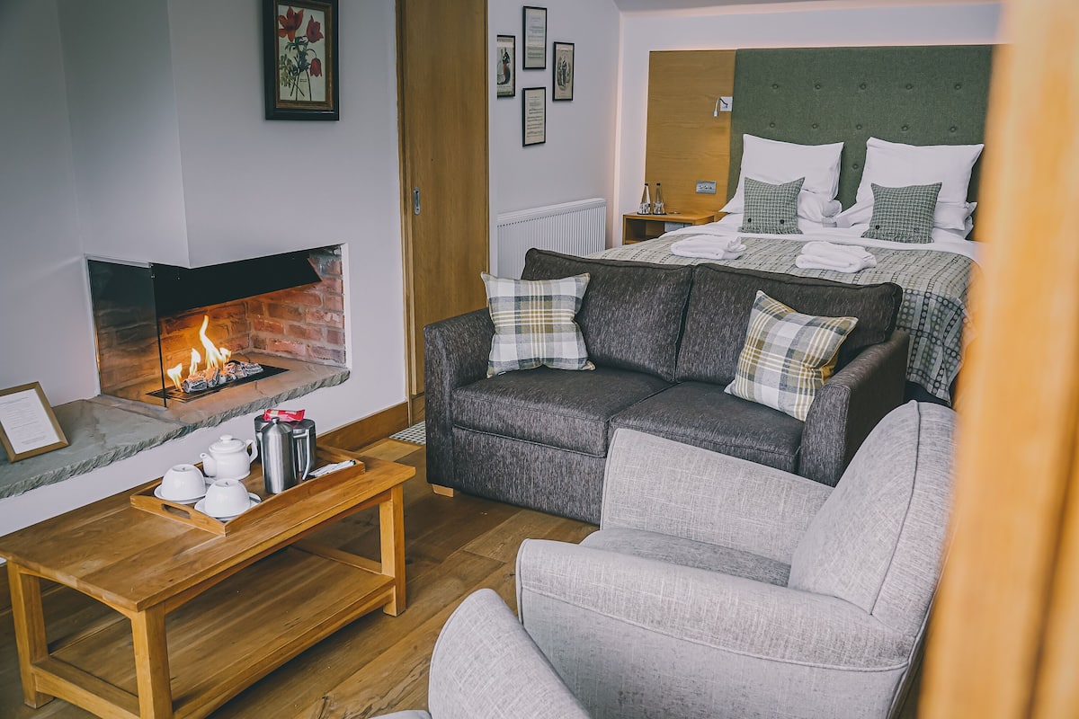A cozy living room with a fireplace, a sofa set, and a bed with a green headboard.