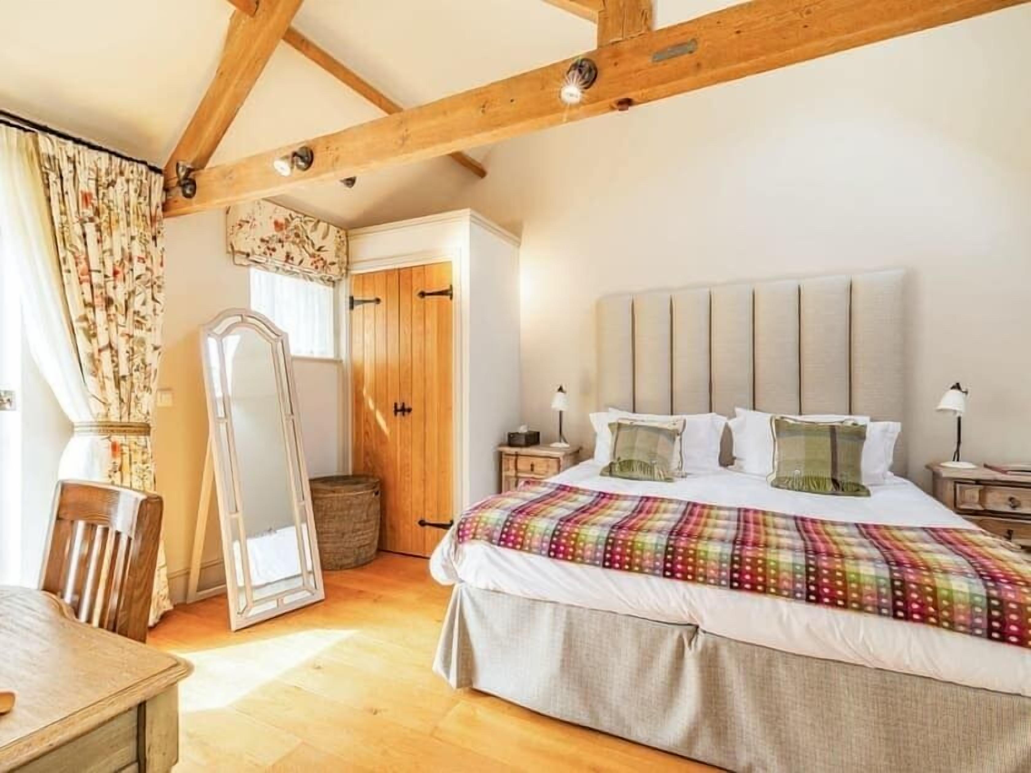 Een slaapkamer met een groot bed, houten balken, een kledingkast en een spiegel.