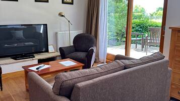 Una sala de estar con sofá, televisor, sillón y mesa. Hay cuadros en la pared y una ventana con cortinas.