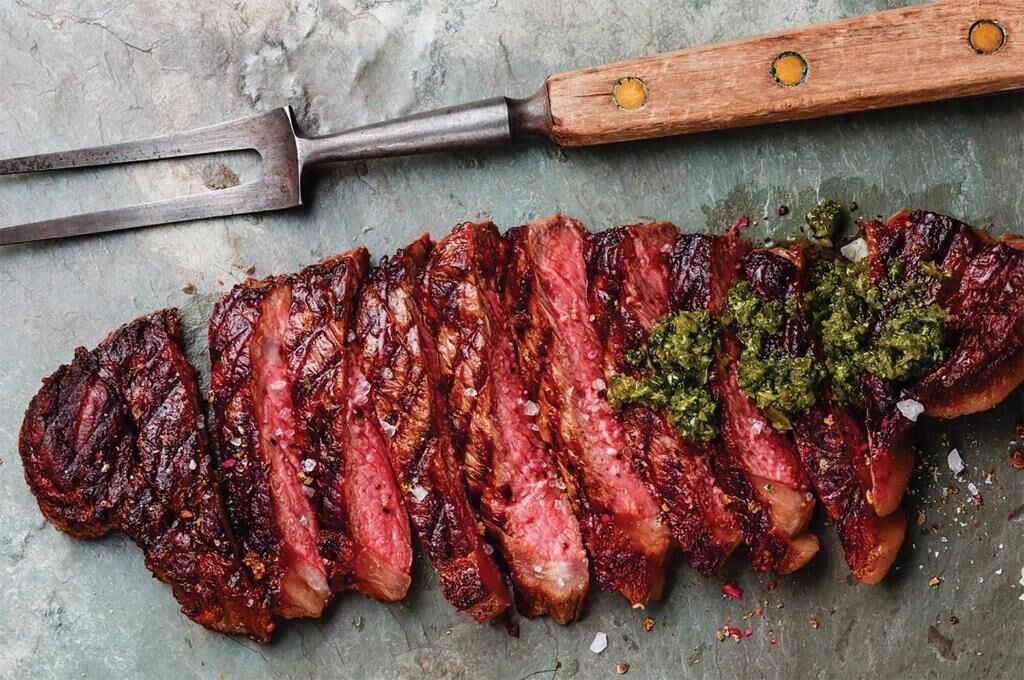 Un steak, une fourchette à viande en bois et une spatule en métal, le tout posé sur une surface texturée.