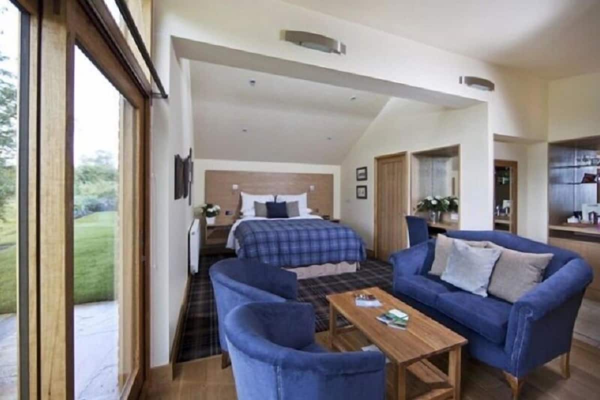 A room with a bed, two blue sofas, a wooden coffee table, and a view of a garden.