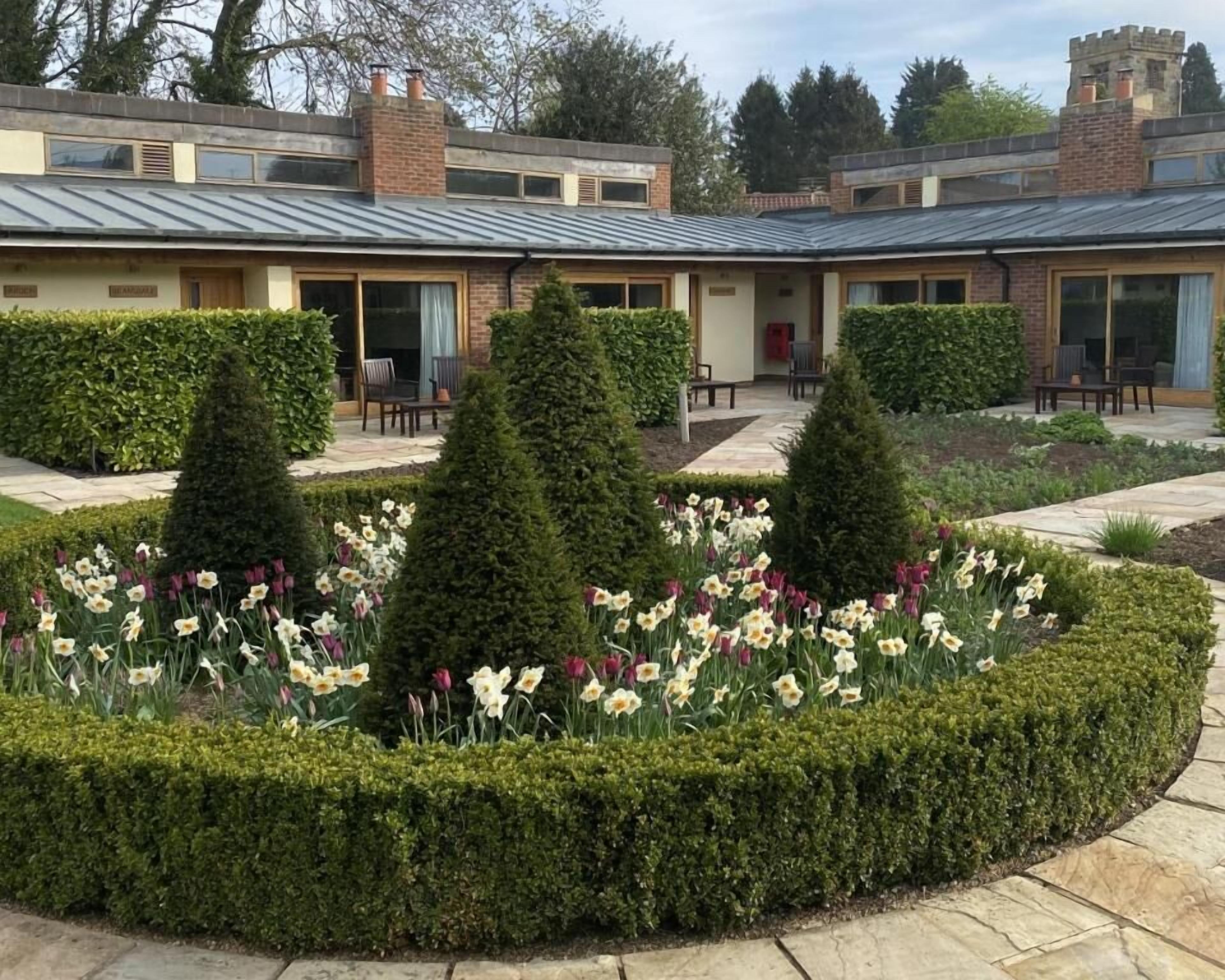 A courtyard with neatly trimmed hedges and a variety of flowers.