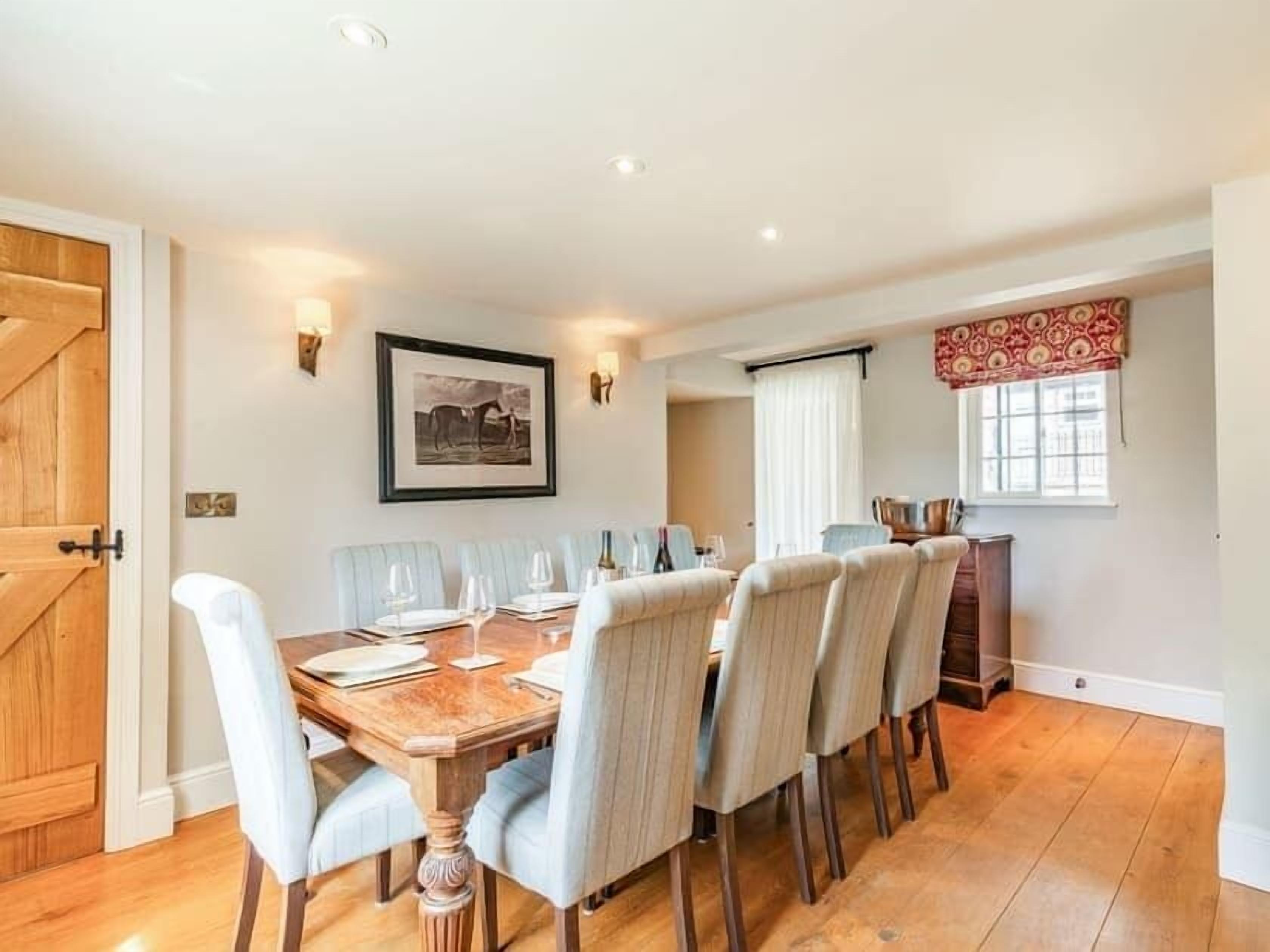 A dining area with a wooden table and six chairs, a framed picture on the wall, and a window with curtains.