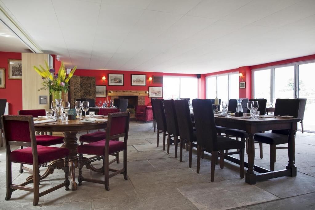 Comedor con paredes rojas, chimenea y varias mesas con sillas.
