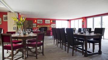 Comedor con paredes rojas, chimenea y varias mesas con sillas.