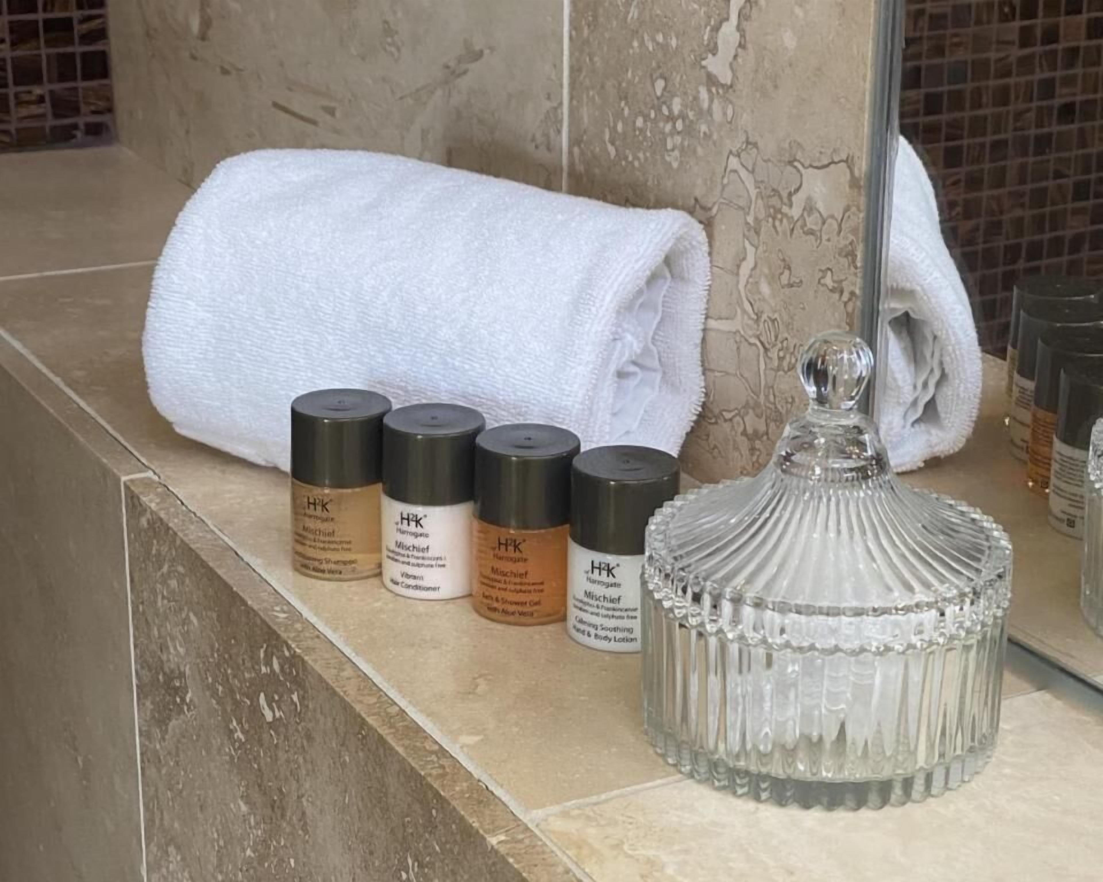 Una encimera de baño con una toalla blanca, cuatro productos para el cuidado de la piel y un recipiente de vidrio.