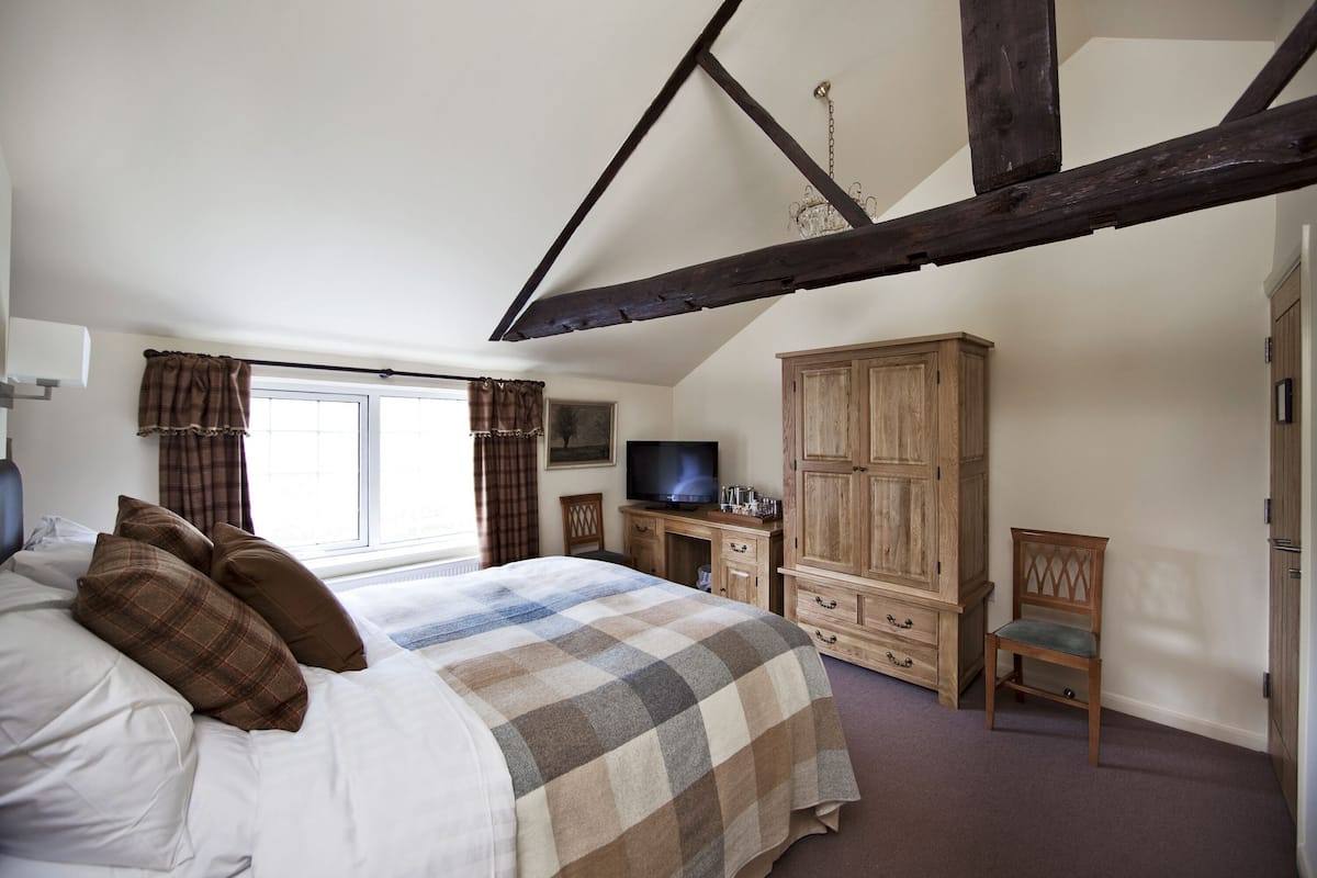 A bedroom with a bed, a television, a wooden wardrobe, and a window.