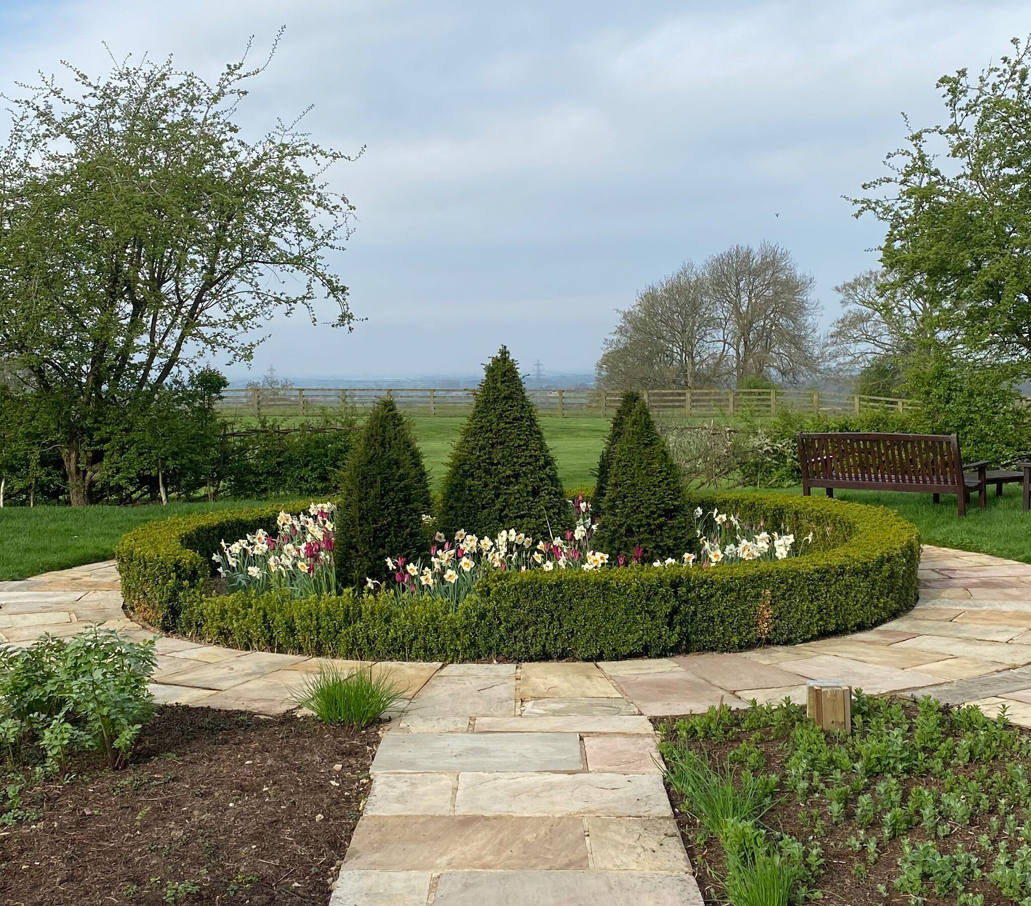A landscaped garden with a stone pathway, neatly trimmed hedges, and a variety of flowers.