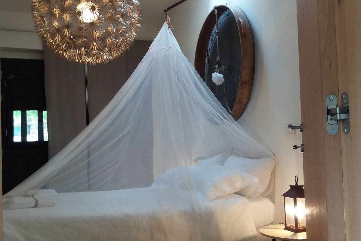 A bed with a white canopy, a round mirror on the wall, and a hanging light fixture.