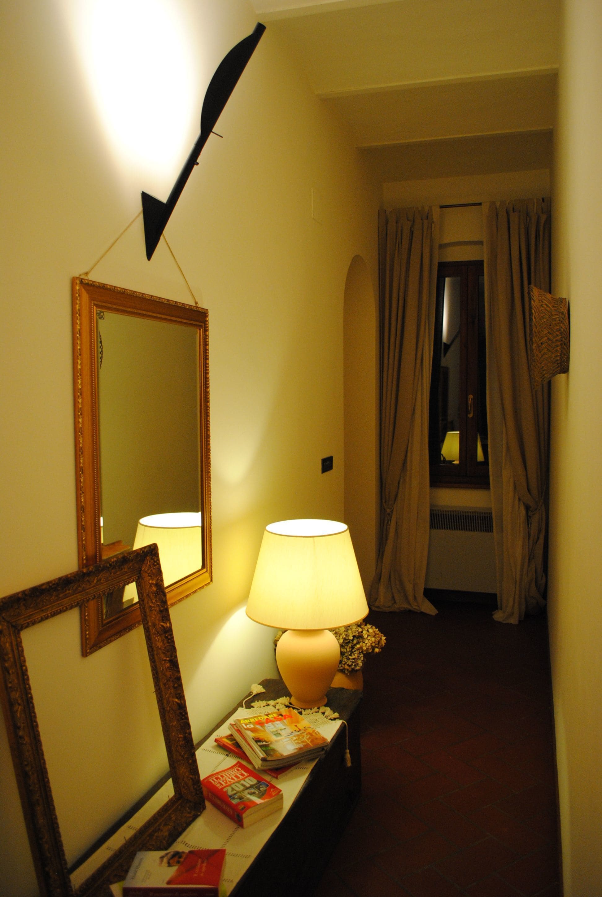 A hallway with a mirror, a lamp, and a table with books.