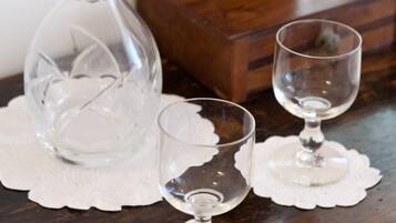 A clear glass decanter and two wine glasses on a wooden table with a lace doily.