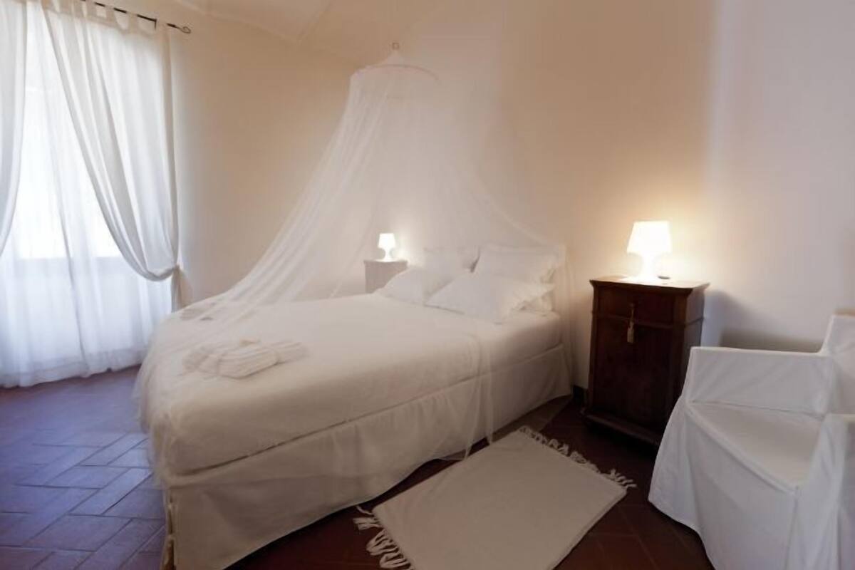 A bedroom with a canopy bed, two bedside tables with lamps, a wooden wardrobe, and a white chair.