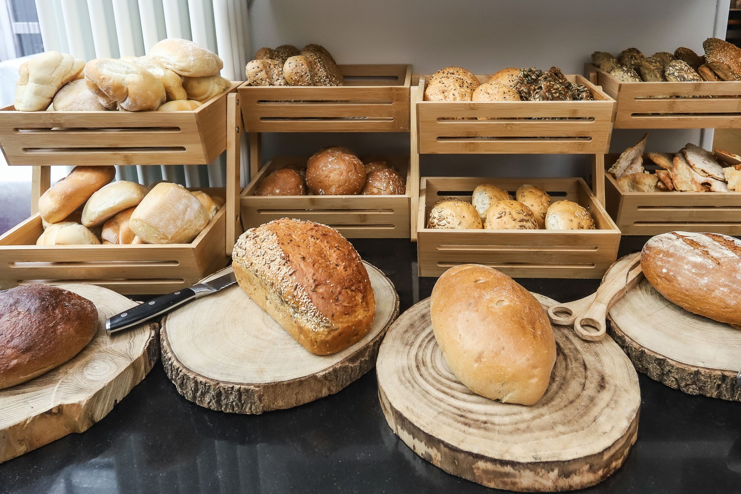 Diferentes tipos de pan expuestos en cajas de madera y sobre tablas de madera.