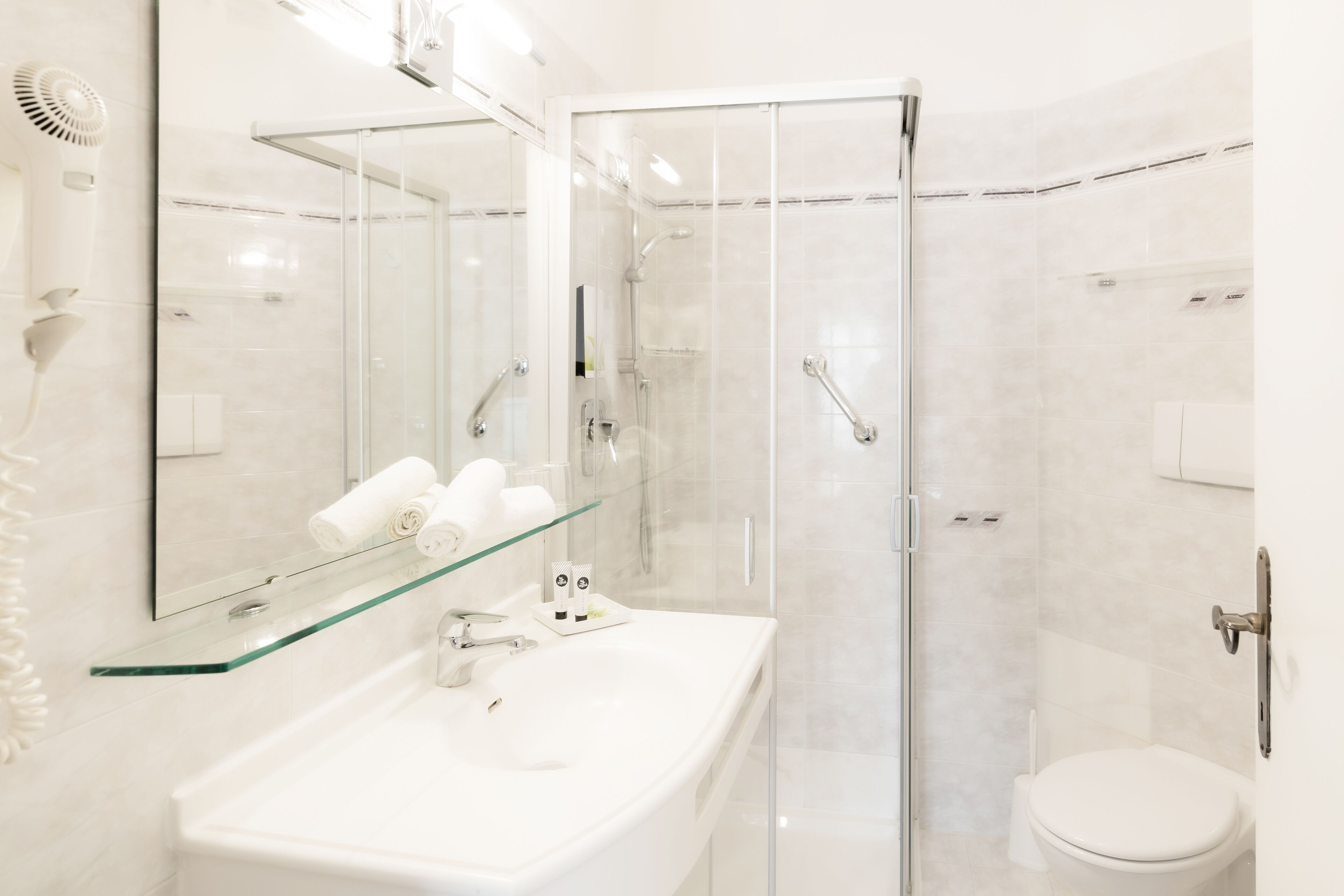 Un baño moderno con cabina de ducha de vidrio, un lavabo blanco con repisa de vidrio y un inodoro.