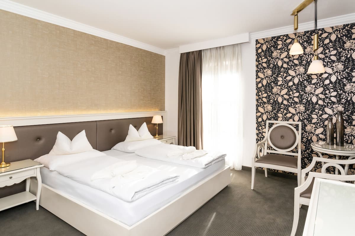 A hotel room with a large bed, two bedside tables with lamps, a chair, and a decorative wall with a floral pattern.
