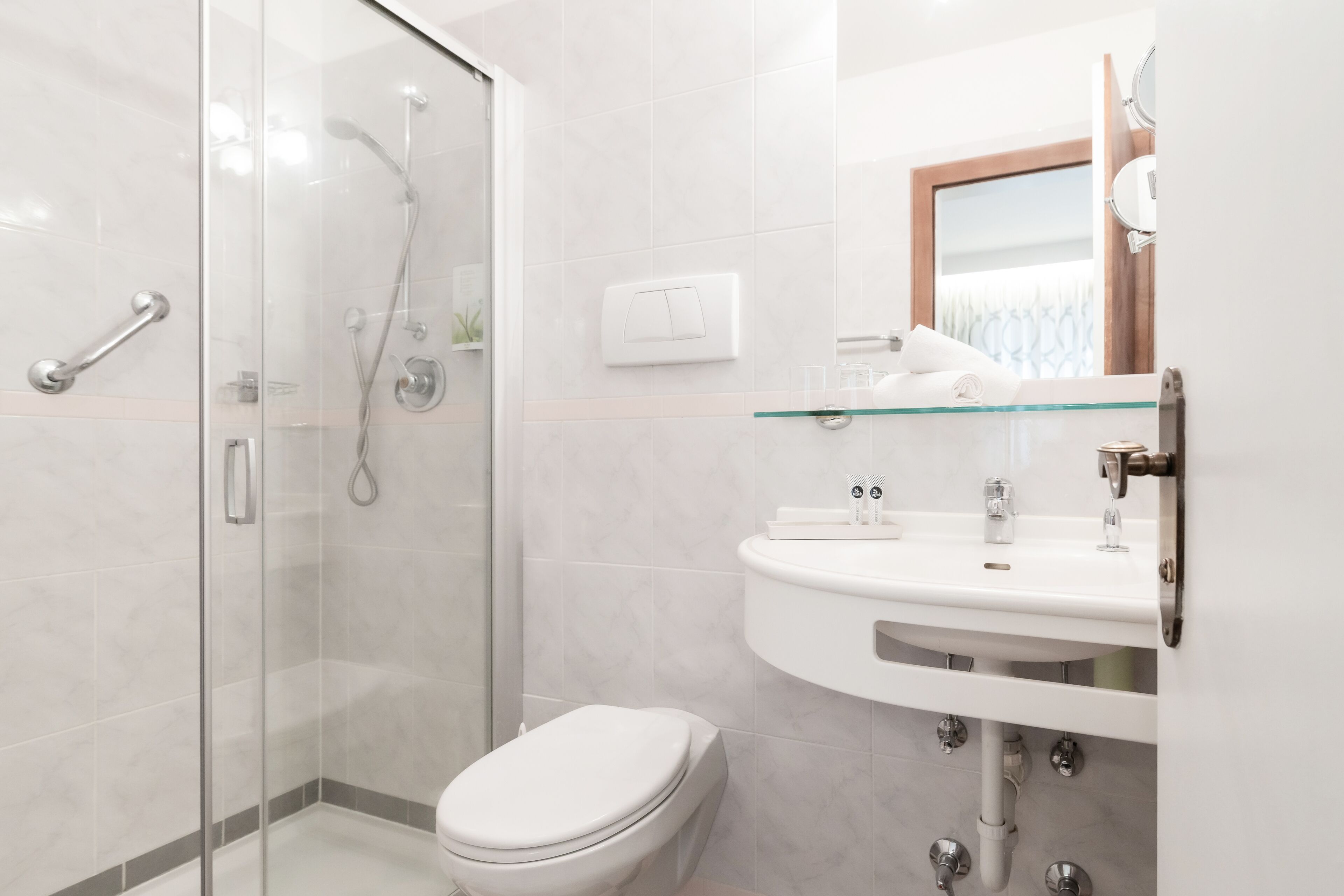 Un baño moderno con cabina de ducha de vidrio, inodoro blanco y lavamanos con espejo.