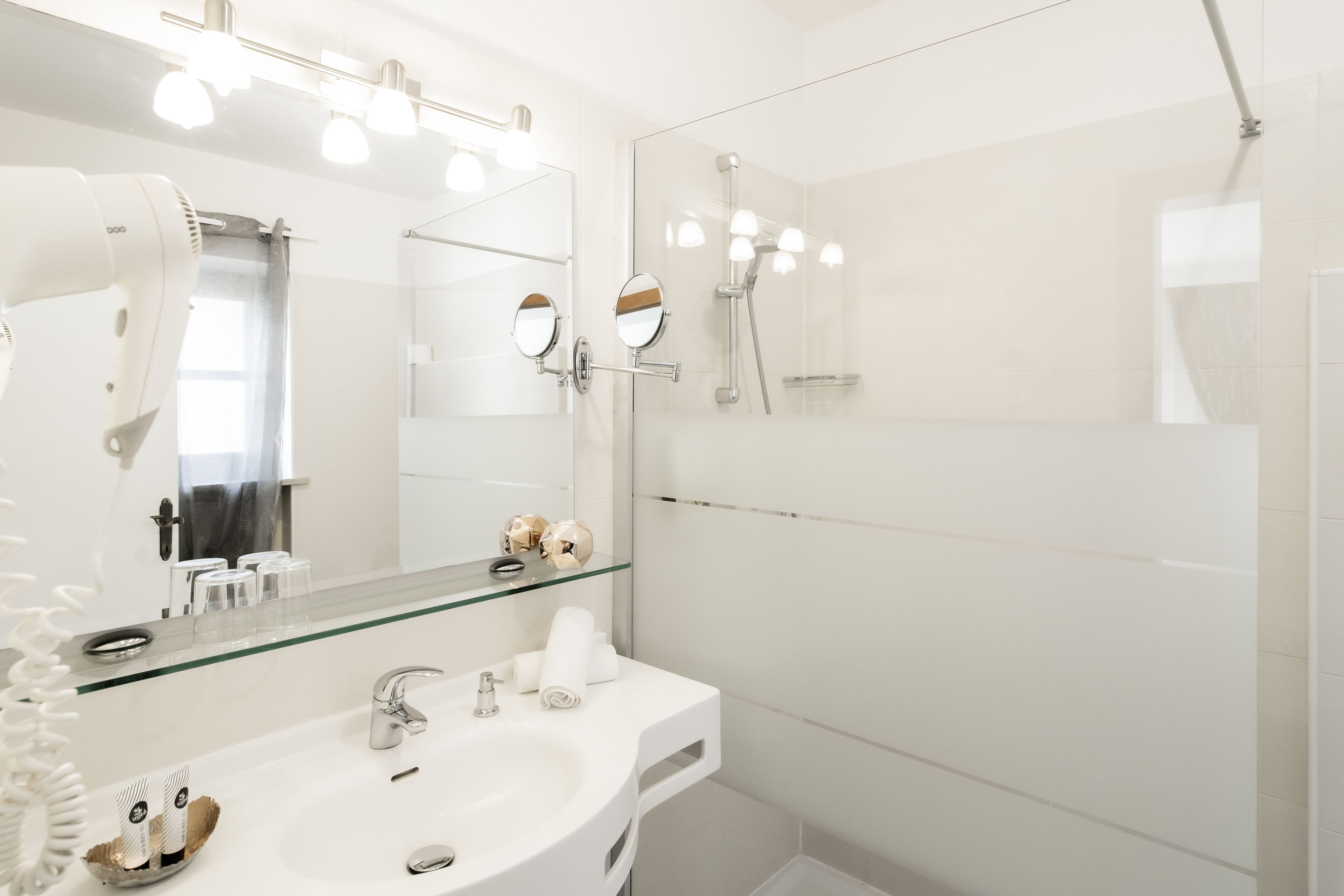 Un bagno moderno con box doccia in vetro, un mobile lavabo con specchio e un asciugacapelli sul ripiano.