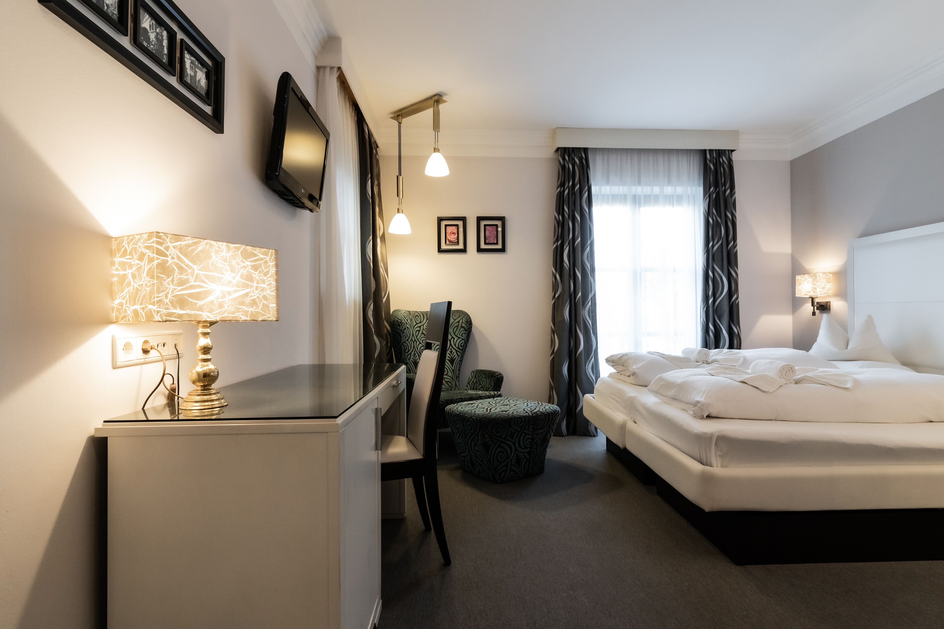 Habitación de hotel con cama, escritorio, silla y televisor en la pared.