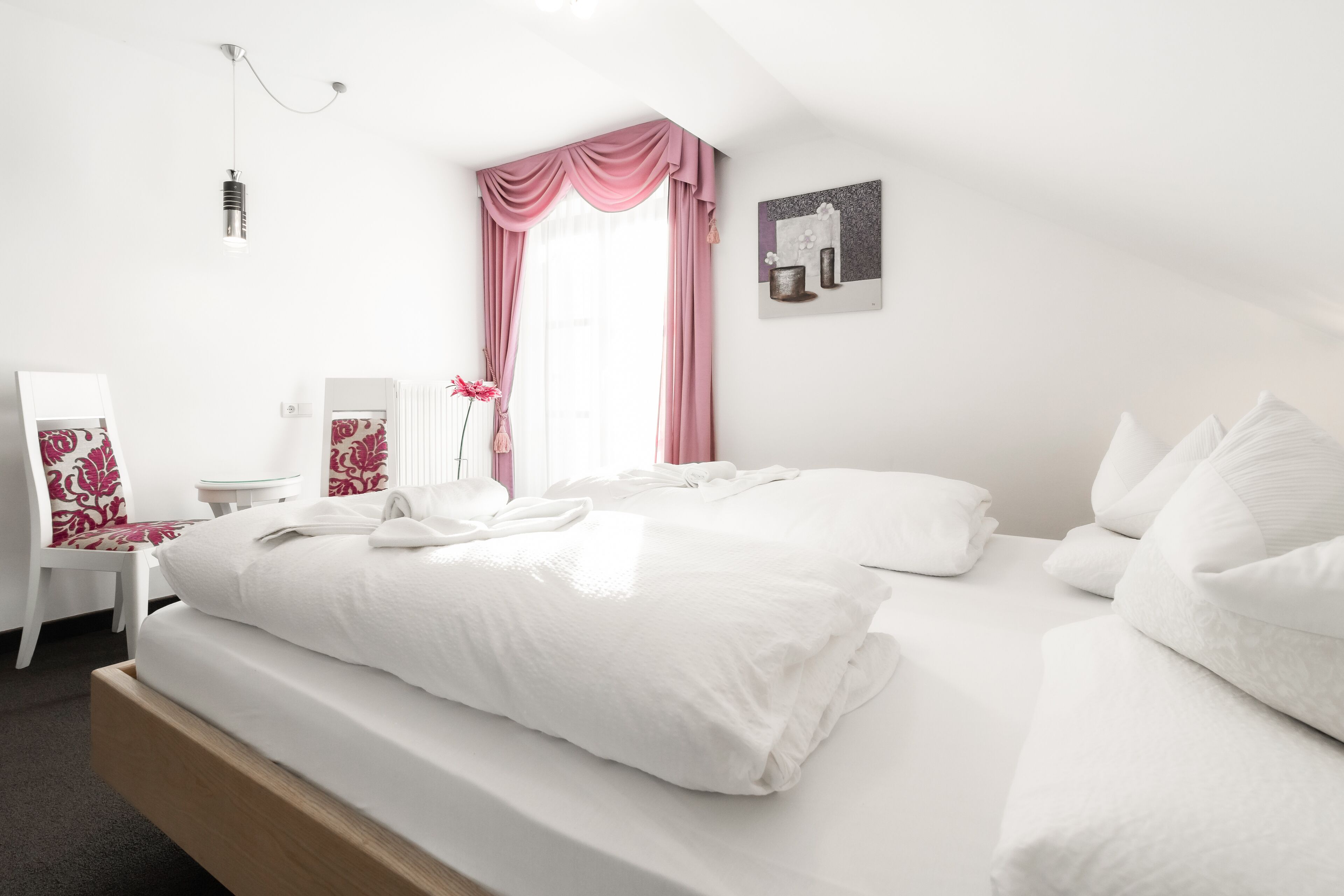 Una cama bien hecha con sábanas blancas, una mesita de noche con una lámpara y una silla con estampado floral.