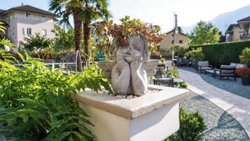 Una estatua de jardín con corona de plantas, rodeada de follaje y un camino empedrado.