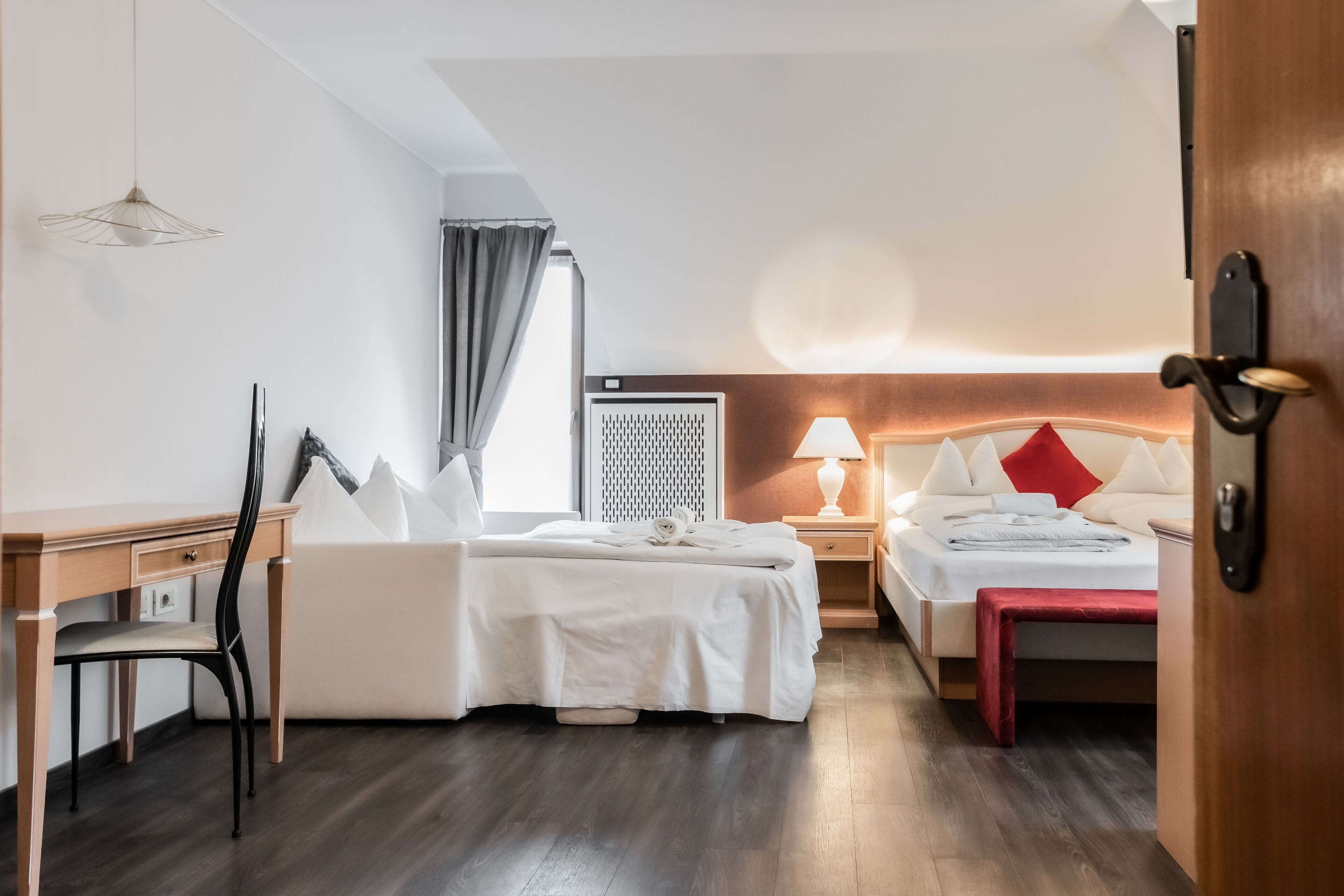 Een hotelkamer met een bed, een bureau, een stoel, een nachtkastje met een lamp en een kledingkast.