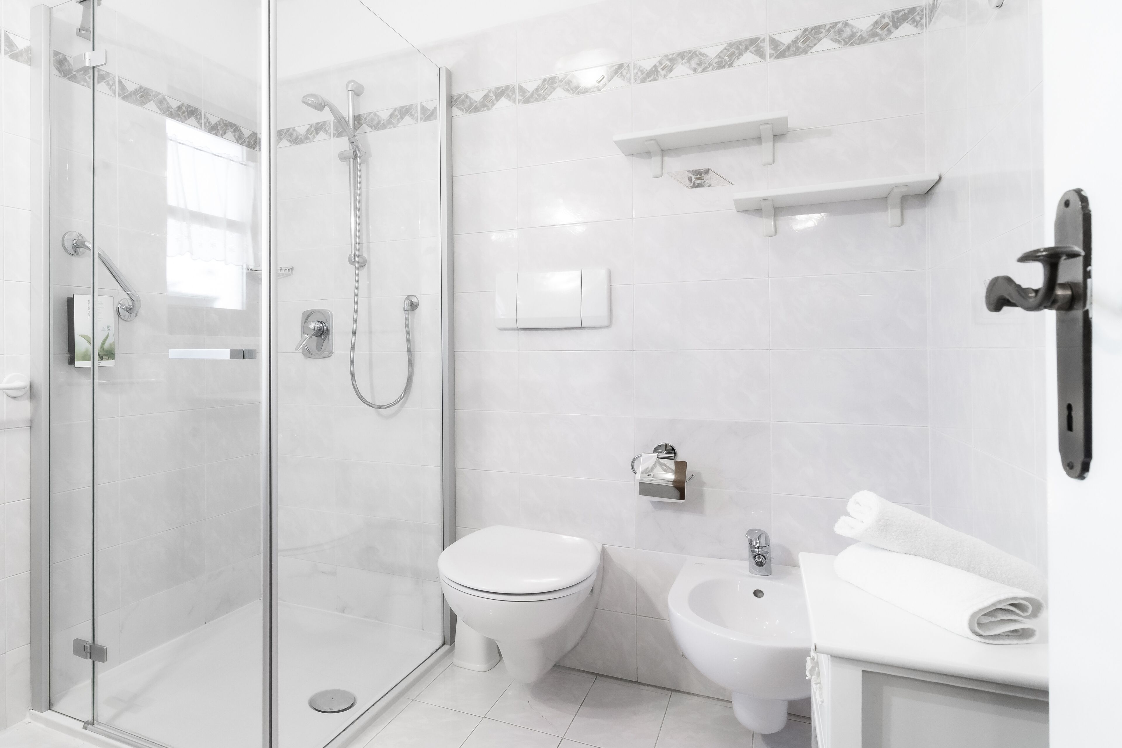 A modern bathroom with a glass-enclosed shower, a toilet, a bidet, and a sink with a towel on the counter.