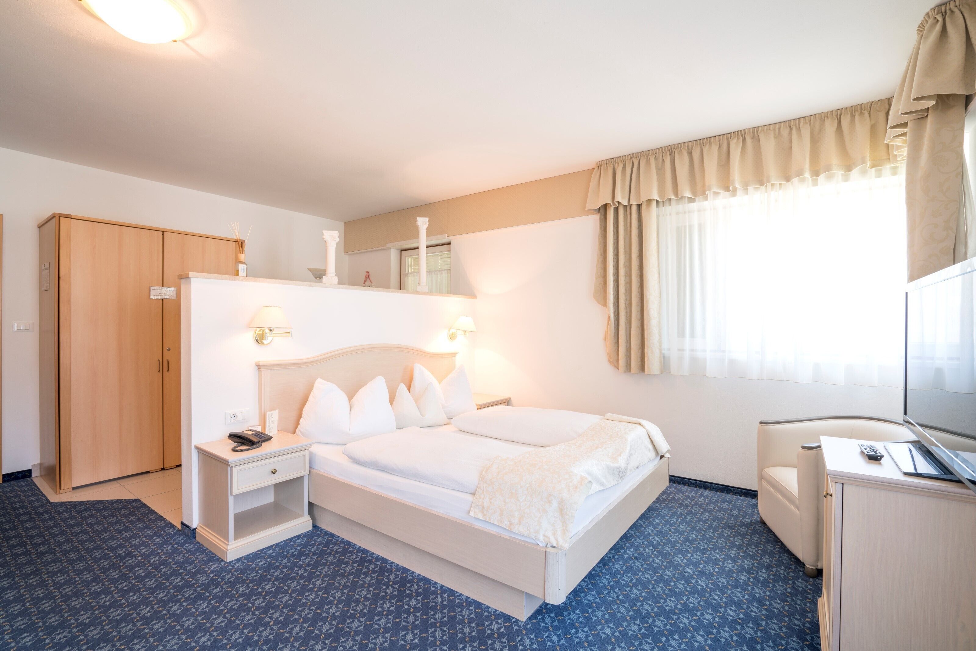 A hotel room with a bed, bedside table, lamp, wardrobe, and a television.