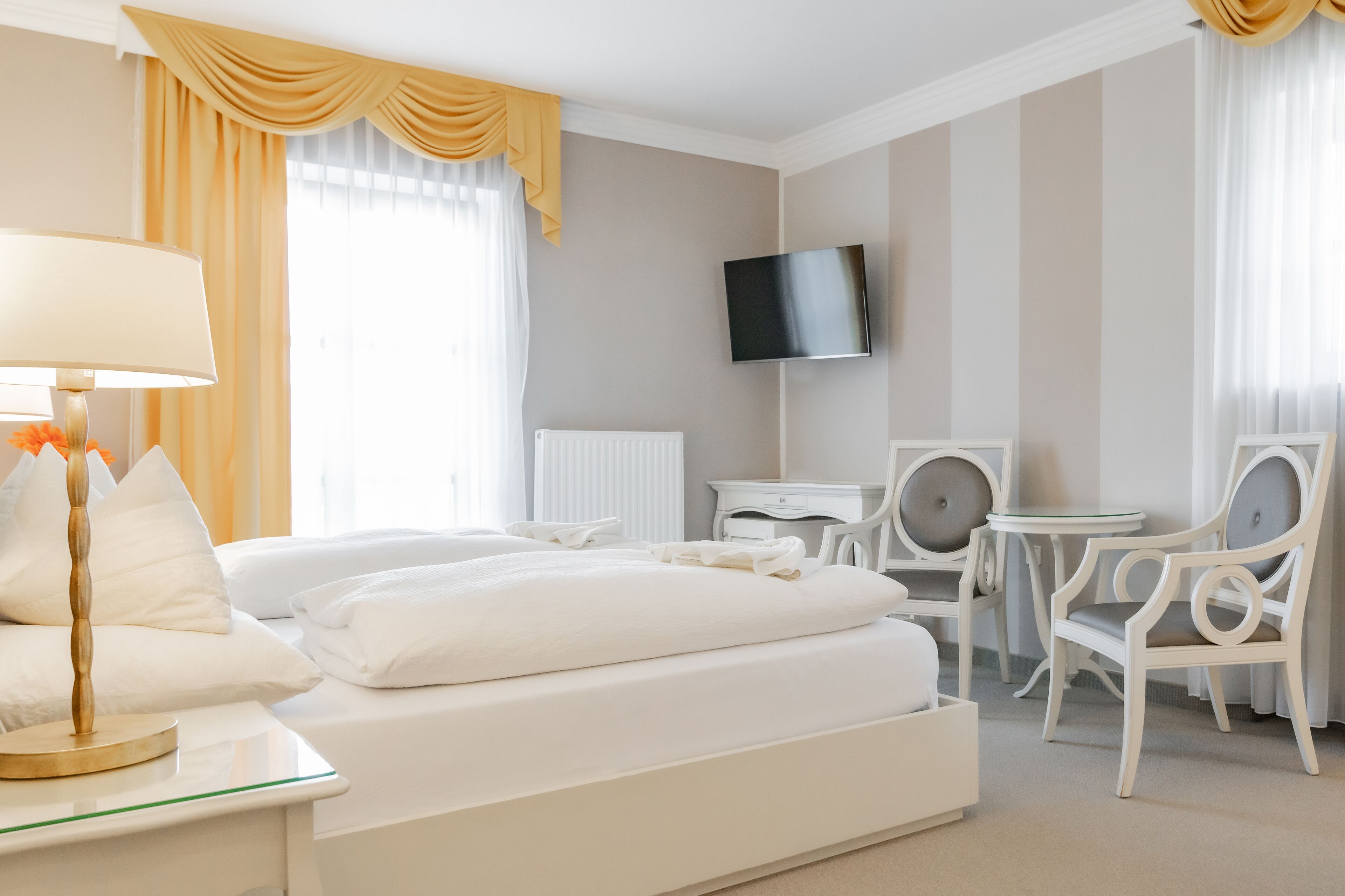 Habitación de hotel con cama, mesita de noche, lámpara, televisor y dos sillas.
