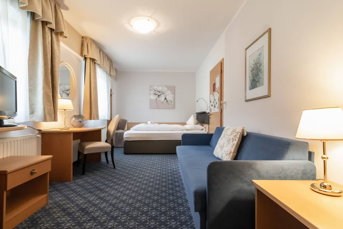 A hotel room with a bed, a desk, a chair, a sofa, and a TV.