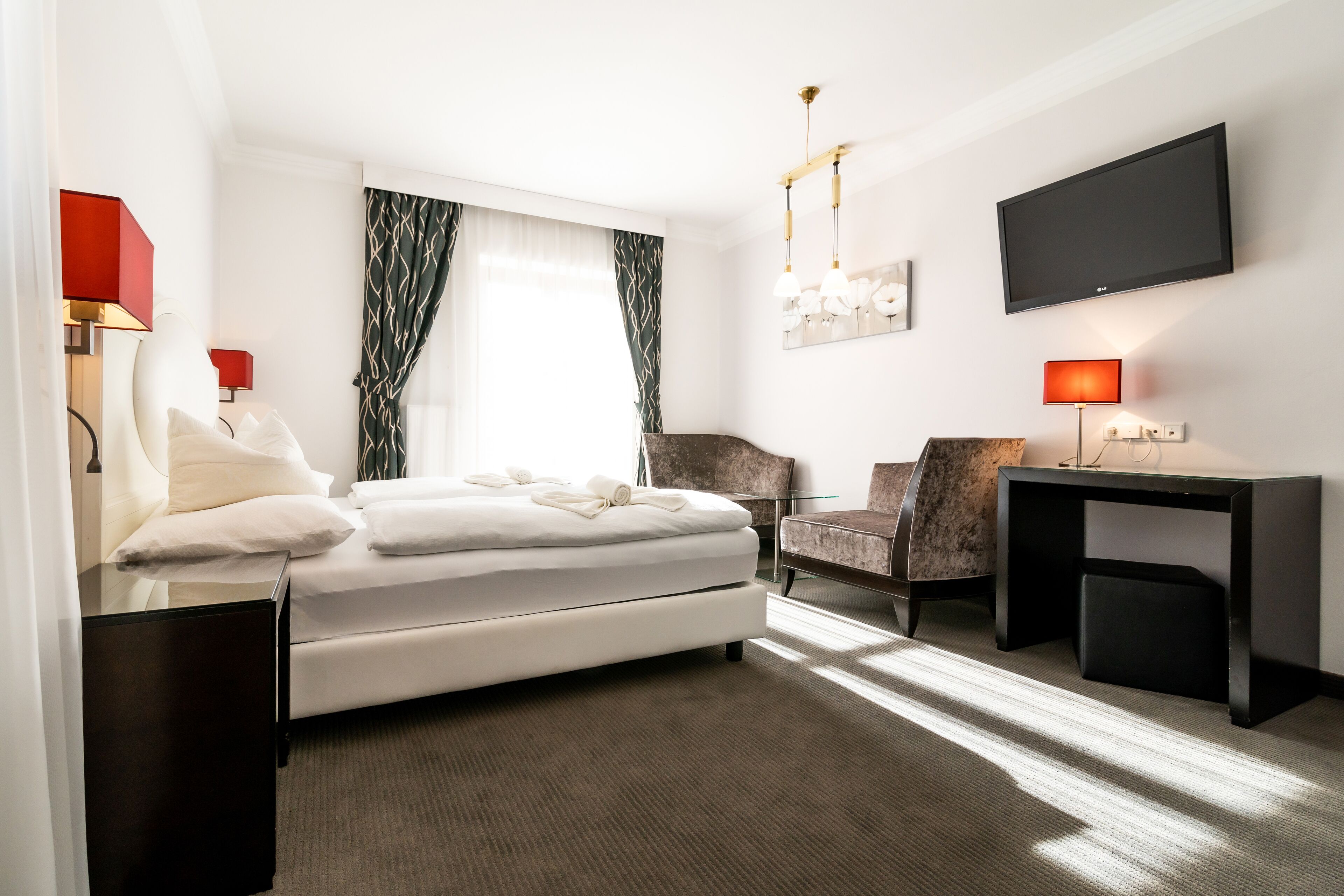 Quarto de hotel moderno com cama, escrivaninha, cadeira e televisão.
