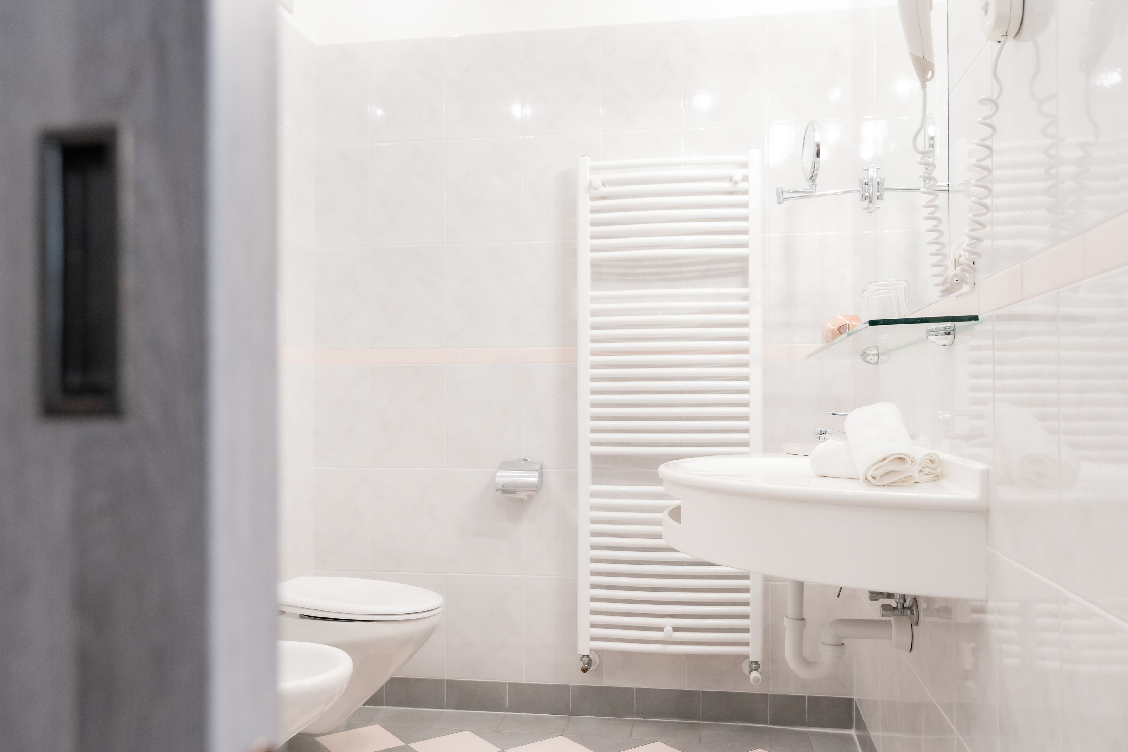 A modern bathroom with a white toilet, a glass shower enclosure, and a white sink with a towel.